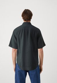 Short-sleeve black shirt made of lightweight fabric, featuring a collar and a curved hem, worn with blue jeans. Simple, textured design.