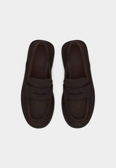 Ζευγάρι σκούρων καφέ δερμάτινων μοκασίνων χωρίς κορδόνια, με ραφές και οριζόντιο λουράκι στο πάνω μέρος, εμφανιζόμενο από πάνω σε λευκό φόντο.
