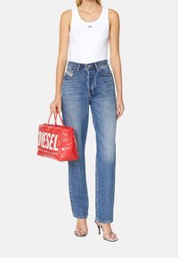 Top blanco sin mangas, jeans azules de tiro alto, bolso rojo hinchado con el logo blanco "DIESEL" y sandalias de tacón alto plateadas.