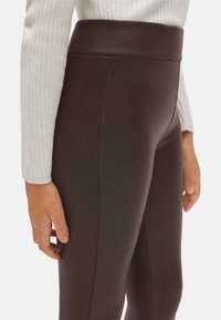 Leggings marrones de cintura alta hechos de material elástico, con una textura suave y un ajuste a medida, mostrados junto a un suéter ligero.