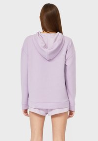 Sudadera morada con capucha, con mangas largas, un corte relajado y puños de canalé. Textura suave y color sólido sin patrones visibles.