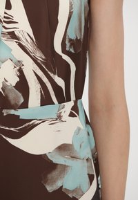 Robe sans manches avec une base marron, présentant des motifs abstraits bleu clair et crème. Tissu lisse avec une taille ajustée.