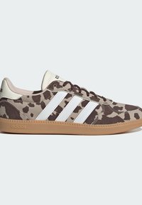 Matalat Adidas-tennarit, joissa on ruskea- ja beigetäpläinen kuvio, valkoiset raidat, ruskeat nauhat ja kumipohja.