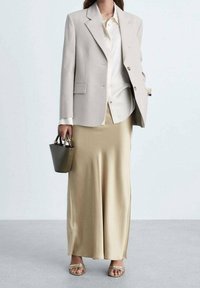 Blazer entallado gris claro, camisa blanca, falda de satén beige, sandalias doradas con tiras y un pequeño bolso de mano verde oscuro con detalles dorados.