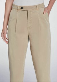 Pantalon plissé beige avec une fermeture éclair, un bouton à l'avant et deux poches latérales, en tissu lisse et léger, avec une coupe ajustée.