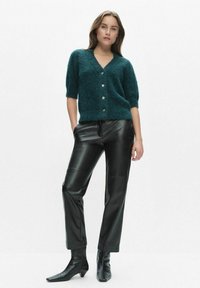 Sinisänkyinen pörröinen neulejakku lyhyillä hihoilla, jossa hopeiset napit, yhdistetty mustiin keinonahkalegginseihin ja kärjellisiin nilkkureihin.