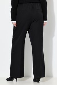 Černé široké kalhoty z měkké látky, s pasem a zadními kapsami. Lem je čistý s jemným faldováním, doplněné černými podpatky.