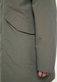 Olivgrön vattentät jacka med en elegant design, som har en tydlig sidficka och en mjuk textur på tyget.