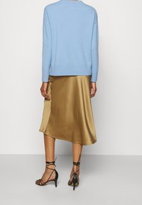 Ljusblå stickad tröja med ribbad nederkant, i kombination med en guldig satinlik asymmetrisk kjol och svarta remsandaler med hög klack.