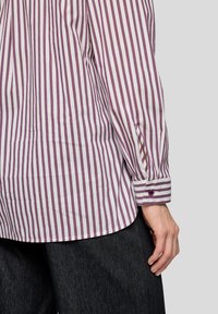 Striped shirt in pale purple and white fabric, featuring a buttoned cuff and a side slit, displayed alongside dark denim pants.