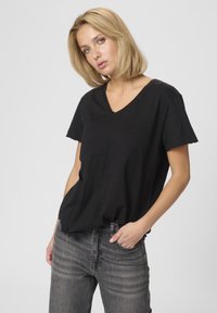 Čierne tričko s V-výstrihom a krátkymi rukávmi, vyrobené z jemného materiálu, v kombinácii s vyblednutými šedými džínsami. Jednoduché, voľné strih, bez viditeľných vzorov.