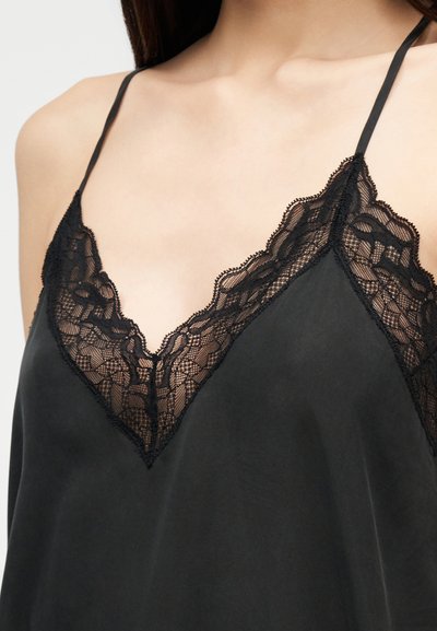 Κοντινό πλάνο μαύρου σατινέ καμιζόλ με λεπτή διακοσμητική δαντέλα με λουλούδια κατά μήκος του βαθιού V-ντεκολτέ και λεπτές τιράντες στους ώμους.