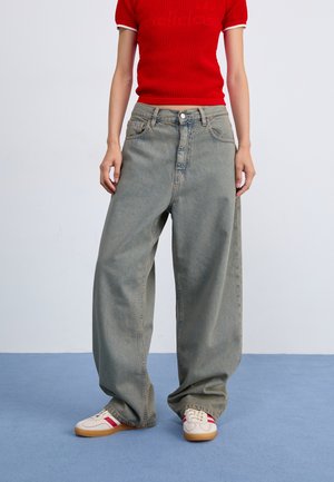 Jeans en denim gris ample avec taille haute, dotés de cinq poches et d'un bouton classique. Assortis avec des chaussures de sport rouges et blanches.