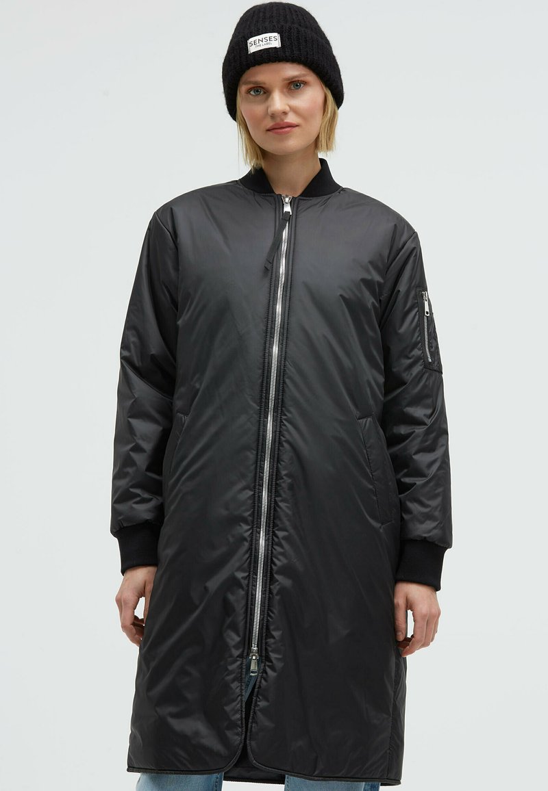 Black long-line bomber jacket made of glossy, lightweight material with a front zipper, side pockets, and ribbed cuffs.