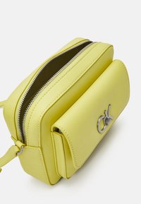 Borsa a tracolla in pelle gialla con chiusura zip, dotata di una patta frontale e un accento in logo argentato. Texture liscia e forma rettangolare compatta.
