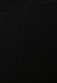 Primo piano di un tessuto nero, che mostra una superficie liscia e una leggera lucentezza. Presenta cuciture visibili lungo le cuciture, creando un aspetto pulito.