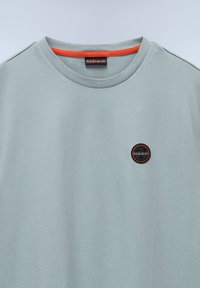 T-shirt in cotone grigio chiaro con scollatura rotonda e dettaglio arancione all'interno. Presenta una patch a forma di cerchio sul davanti. Tessuto morbido.