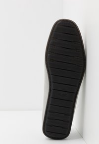 Semelle de chaussure en daim gris avec un grip en caoutchouc noir texturé et le logo 'HUGO' embossé. Le talon présente de subtils accents marron.