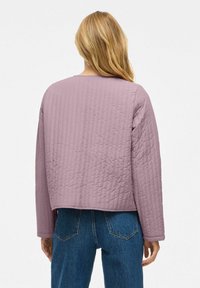 Quiltad, lätt jacka i dämpad lavendel. Har långa ärmar, rund halsringning och en kortad fåll. Bärs över högmidjade jeans.
