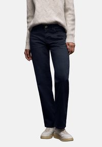 Vaqueros rectos de denim azul oscuro, con cierre de botones, trabillas para cinturón y bolsillos traseros, combinados con un suéter de punto color crema.