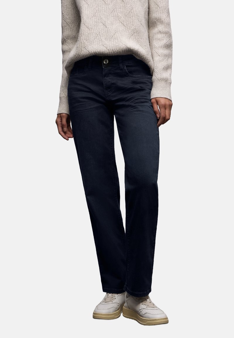 Vaqueros rectos de denim azul oscuro, con cierre de botones, trabillas para cinturón y bolsillos traseros, combinados con un suéter de punto color crema.