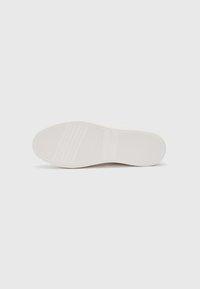 Sole di sneaker bianca con una superficie liscia, scanalature orizzontali e verticali, e una lieve curvatura sulla punta. L'etichetta riporta "Tommy Hilfiger."