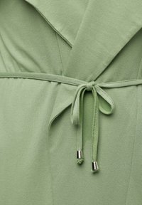 Grünes Stoffwickelkleid mit einem Taillengürtel und gebundenem Detail sowie metallischen Akzenten. Weicher Stoff mit glatter Oberfläche und geschichtetem Design.