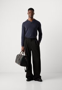Suéter de manga larga color marino, pantalones de pierna ancha negros y un bolso de lona bicolor de cuero con detalles en marrón. Texturas suaves en todo.