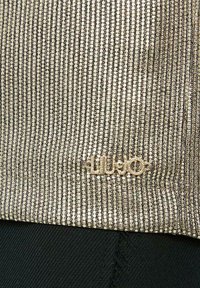 Top metallico oro con un motivo testurizzato, linee verticali e un piccolo logo argentato "Liu Jo" all'orlo. Tessuto nero sotto.