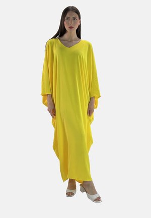 Abito giallo ampio realizzato in tessuto leggero, caratterizzato da una profonda scollatura a V e maniche larghe, abbinato a tacchi aperti bianchi.