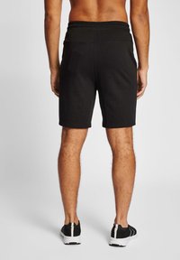 Shorts de sport noirs avec une taille élastique, longueur genoux, tissu lisse et détails de couture minimes, associés à des chaussures noires.