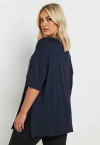 Marinblå överstor topp med korta ärmar, med sidospalter och en mjuk, slät textur. Enkelt och rent design utan dekorationer.