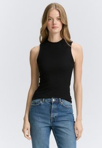 Schwarzes, geripptes, ärmelloses Oberteil mit hohem Kragen, kombiniert mit hellblauen, hoch taillierten Jeans. Glatter Stoff und figurbetonter Schnitt.