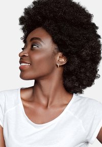 Profil af en person med voluminøst sort naturligt hår, iført en hvid T-shirt, med en lille guld-hoopørering og glat hud.