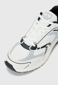 White athletic sneakers featuring mesh fabric, black and grey accents, a padded collar, and a prominent logo on the tongue.