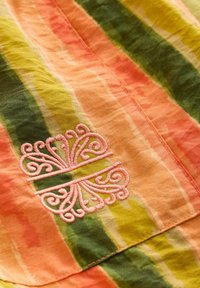 Multicolored fabric featuring horizontal stripes in orange, green, and yellow. Pink embroidered decorative pattern at the bottom.