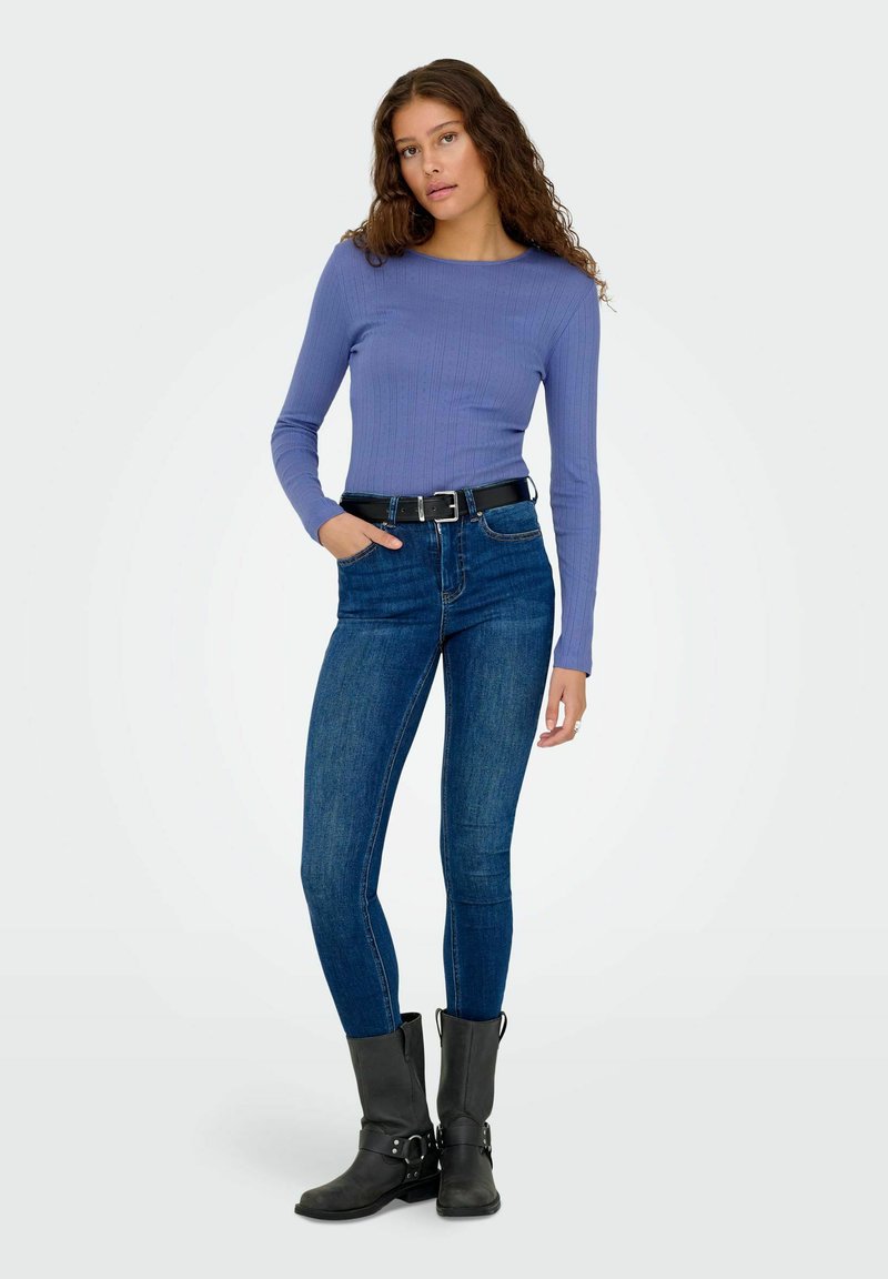 Langærmet, ribbet, lilla top kombineret med mørkeblå skinny jeans. Et sort bælte og sorte ankelstøvler med spænder fuldender outfittet.