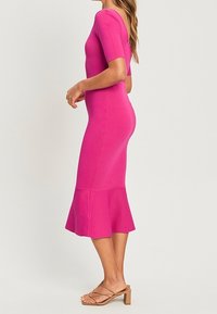 Abito aderente a maniche corte in un vivace tessuto knit rosa, con orlo svasato e una texture liscia, abbinato a sandali con cinturini.