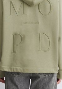 Olivgrön hoodie med präglade bokstäver "M O P D" och "MARC O'POLO DENIM." Har en känguruficka och ribbad nederkant.