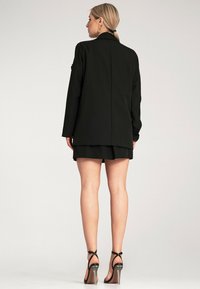 Czarny żakiet o dopasowanym kroju, z długimi rękawami, z klapami; noszony z dopasowanymi szortami. Szpilki dopełniają stylizację.