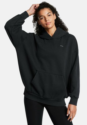Black oversized hoodie made of soft fabric, featuring a front pocket, ribbed cuffs, and a drawstring hood. Simple design with minimal branding.