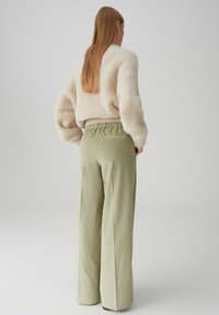 Cremfarbener, flauschiger Pullover kombiniert mit hoch taillierten, hellgrünen, weit geschnittenen Hosen mit vertikalen Streifen und einem elastischen Bund.