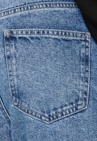 Ljusblå denimjeans med en bakficka i en klassisk rektangulär form, synlig sömnad och en lätt blekt textur.