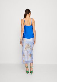 Blå satin camisole med tunna band, i kombination med en genomskinlig, ljusblå kjol med moln- och cherubmotiv, kompletterad med gröna högklackade sandaler.