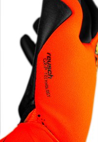 Gant orange vif avec des accents noirs, en tissu texturé et détail gravé "Reusch Grip Technology". Conçu pour améliorer la prise.