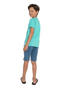 Turquoise katoenen T-shirt met korte mouwen, gecombineerd met blauwe denim shorts. Het kind staat zijwaarts, met zwarte slippers aan.