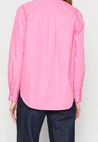 Långärmad skjorta i klar rosa bomull med rundad nederkant, knäppta manschetter och detaljer med veck på ryggen.