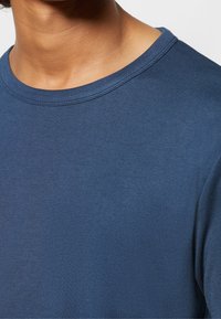Gros plan d'une personne portant un t-shirt bleu à col rond, montrant le col et la partie supérieure de la poitrine.
