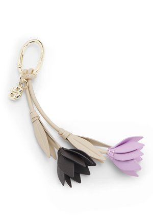 Avainketju, jossa on kullanvärinen rengas ja beiget nahkalenkit, joihin roikkuu kaksi kukkakoruja, yksi musta ja yksi laventelinvärinen, jokaisessa kerrokselliset terälehdet ja lehdet.