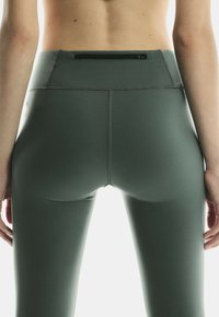 Hoch taillierte, dunkelgrüne Leggings aus elastischem Stoff, mit einer kleinen Reißverschlusstasche auf der Rückseite und flachen Nähten für Komfort.